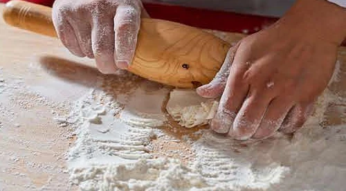 Rolling the scalded wrapper with the 走槌 on the floured board.